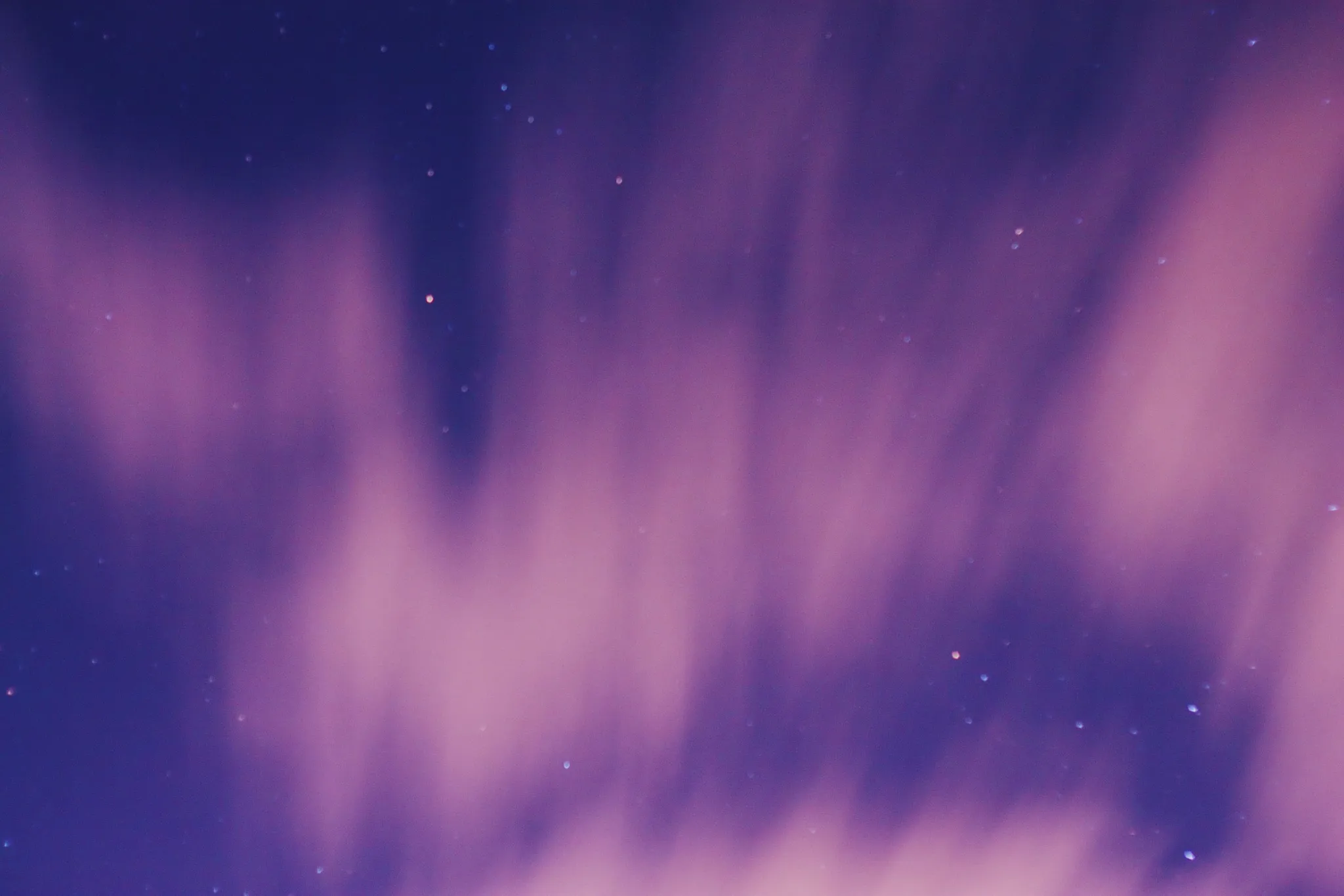 A pink and violet aurora beneath a starry sky